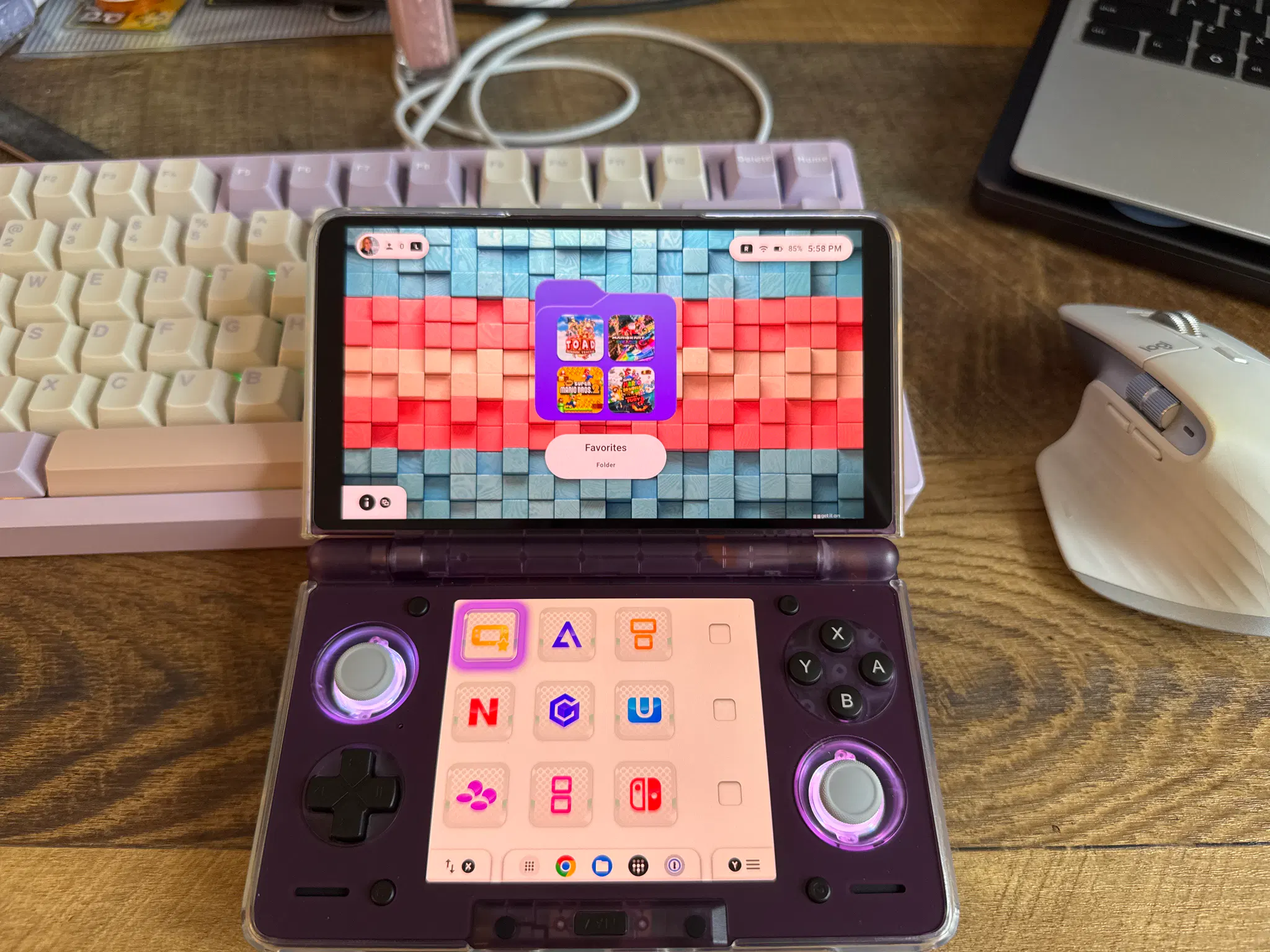 an ayn thor sitting on a desk in front of a pastel purple keyboard. it's running the cocoon launcher with the background set to the trans pride 2025 wallpaper from wallaroo